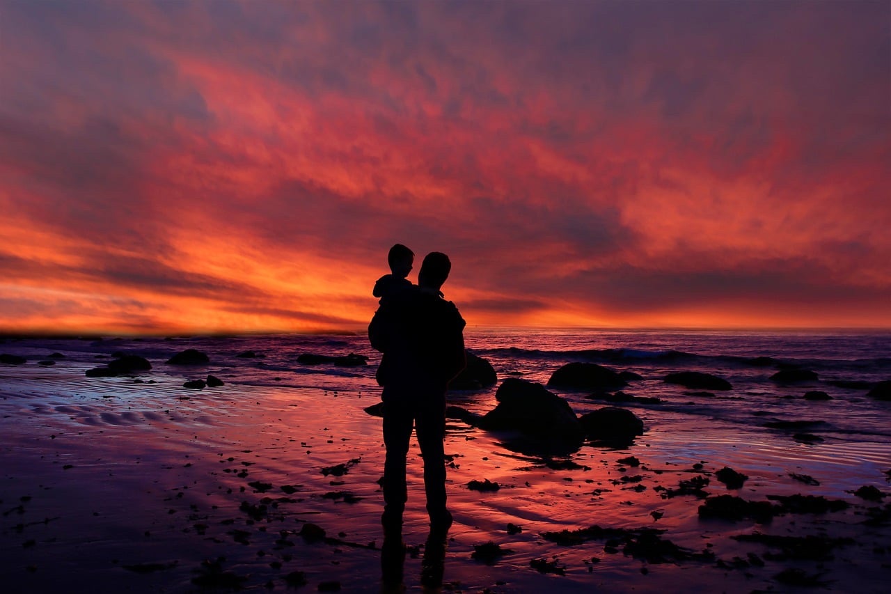 家族が夕暮れの浜辺で過ごすシルエット、子育て世帯の控除拡充をイメージ